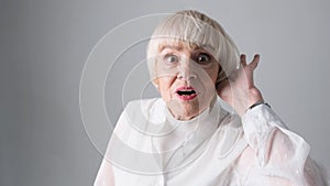 Surprised elderly woman with wide-open eyes on a white background.