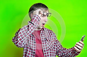 Surprised and excited man with open mouth in red checkered shirt putting on glasses on forehead and looking at smartphone
