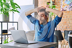 Surprised excited overjoyed young handsome man looking at laptop sitting in cafe