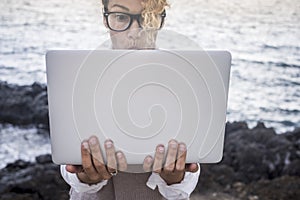 Surprised face expression for beautiful caucasian young woman work on a laptop in alternative office outdoor on the coastline near