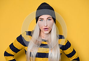 Surprised face of woman stare to camera, model wearing woolen cap and sweater, isolated on yellow background. Surprise expression