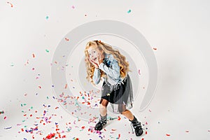 Surprised fashionably dressed curly hair tween girl in in denim jacket and black tutu skirt and rough boots on white background