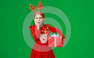 Surprised funny child girl in   Christmas reindeer costume with big gift on green background
