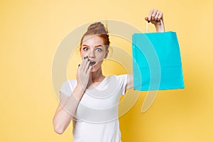 Surprised ginger woman holding packet in hand and covering mouth