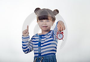 Surprised girl in dress with red clock on white background. Shocked kid holding alarm clock.