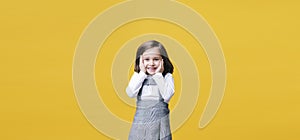 A surprised girl with hands on her face on yellow background