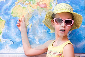 Surprised girl in a hat and sunglasses shows on a world map