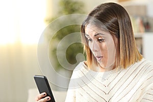 Surprised girl holding smart phone at home