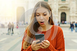 Surprised girl looks at mobile phone in city square in autumn photo