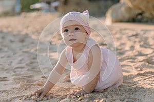 Surprised girl in outdoor with sunset light. Baby in pink dress on sandy beach