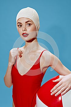 Surprised girl in a red swimsuit swimming cap posing with a ball