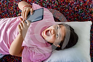 Surprised girl with smart phone lying on the carpet