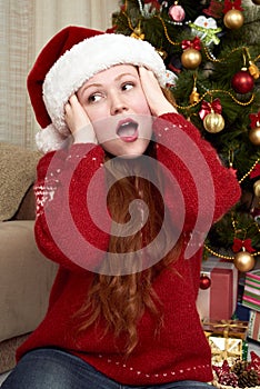 Surprised girl touch head. Home interior with christmas decoration, fir tree and gifts. New year eve and winter holiday concept.