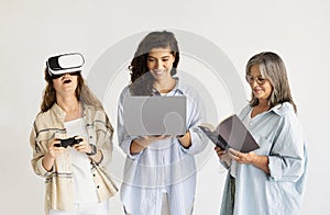 Surprised glad millennial, elderly women and teen girl in VR glasses with phone, laptop and book