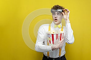 surprised guy in festive outfit in 3d glasses watches movie with popcorn and looks at copy space, student cinema viewer