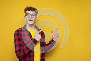 Surprised guy student with curly hair with hands shows space for text, nerd advertises copy space