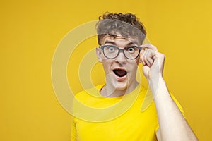 Surprised guy student with curly hair holding glasses and looking, cute nerd in glasses on yellow background