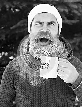 Surprised handsome man in santa claus hat, bearded hipster with beard and moustache drinks from cup with good morning