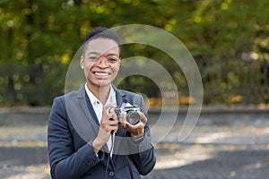 Surprised and happy African American woman looks at the camera and smiles holding a film camera on a walk in the park