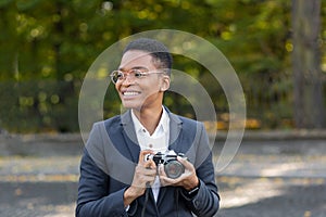 Surprised and happy African American woman looks at the camera and smiles holding a film camera on a walk in the park