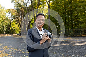 Surprised and happy African American woman looks at the camera and smiles holding a film camera on a walk in the park