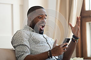 Surprised happy african man looking at cellphone read good news photo