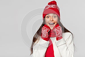 Surprised happy beautiful woman looking sideways in excitement. Christmas girl wearing knitted warm hat and mittens, isolated on g