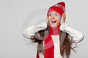 Surprised happy beautiful woman looking sideways in excitement. Christmas girl wearing knitted warm hat and scarf, isolated on gra