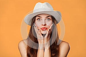 Surprised happy beautiful woman looking sideways in excitement. Excited girl in hat, isolated on orange background