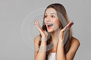 Surprised happy beautiful woman looking sideways in excitement. Isolated on gray background