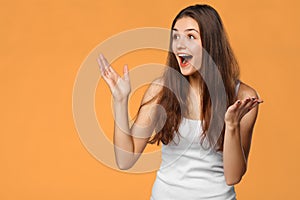 Surprised happy beautiful woman looking sideways in excitement, isolated on orange background