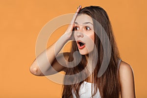 Surprised happy beautiful woman looking sideways in excitement. Isolated on orange background.