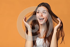 Surprised happy beautiful woman looking sideways in excitement. Isolated on orange background