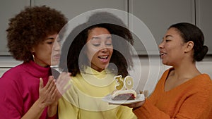 Surprised happy black woman making wish and blowing candles on birthday cake