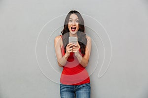 Surprised happy brunette woman in casual clothes holding smartphone