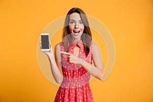 Surprised happy brunette woman in dress showing blank smartphone screen