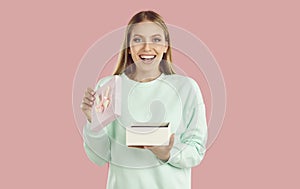 Surprised happy smiling blondy girl in mint sweatshirt opened giftbox present on pink background. photo