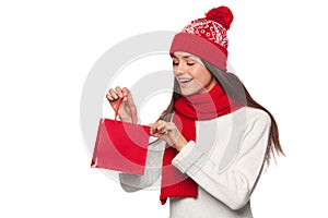 Surprised happy woman holding and looks in red bag in excitement, shopping. Christmas girl on winter sale with gift, isolated