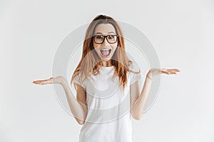 Surprised happy woman in t-shirt and eyeglasses shrugs her shoulders