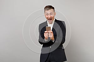 Surprised happy young business man screaming keeping mouth open wide, using mobile phone typing sms message isolated on