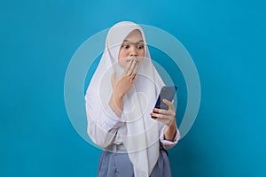 Surprised high school girl looking at smartphone covering her mouth