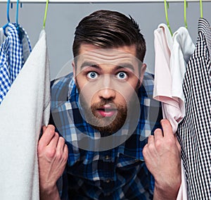 Surprised hipster man standind near rack with clothes