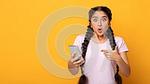 Surprised indian woman using mobile phone, pointing at gadget