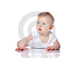 Surprised intrigued infant baby boy with blue eyes is lying on his stomach looking at copy space on white