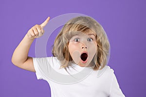 Surprised kid boy pointing up finger on blue background. Shocked kid pointing to copyspace, showing promo offers, points