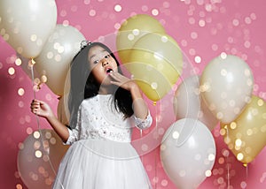 Surprised kid girl with balloons in princess dress with tiaraholds balloon. golden spangles