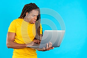 Surprised latin man with dreadlocks using a laptop