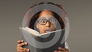 Surprised little black girl with book at gray background