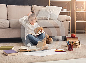 Surprised little female child hugging her teddy bear and reading