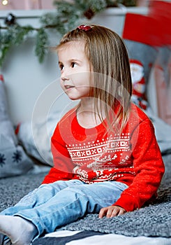 A surprised little girl in Christmas clothes looks away